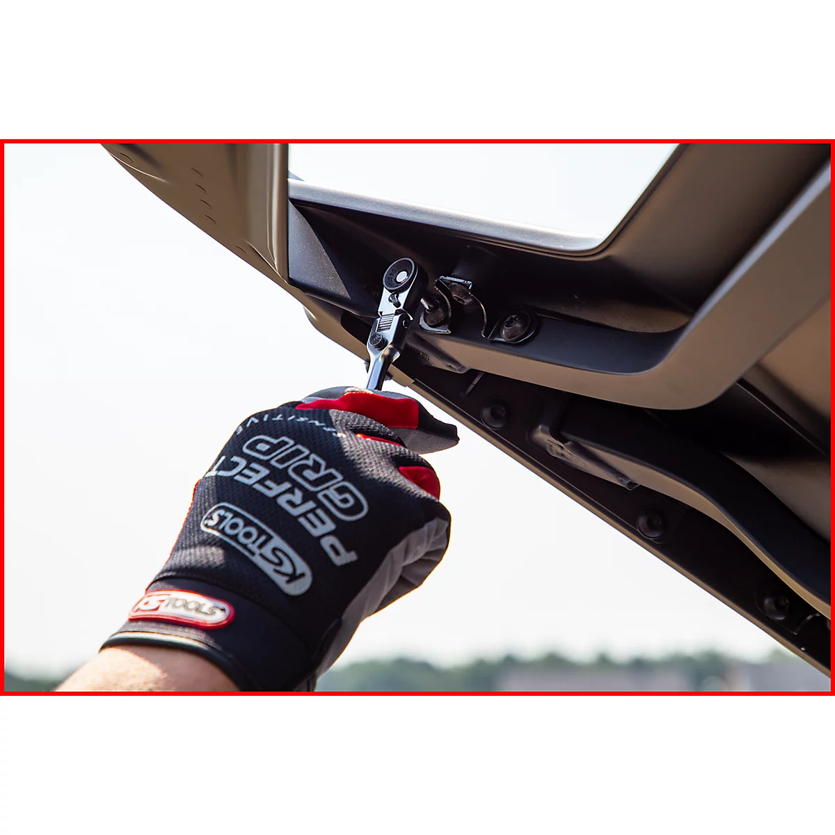 Person mit Handschuh mit Schriftzug PERFECT GRIP schraubt mit Werkzeug an Fahrzeugteil.